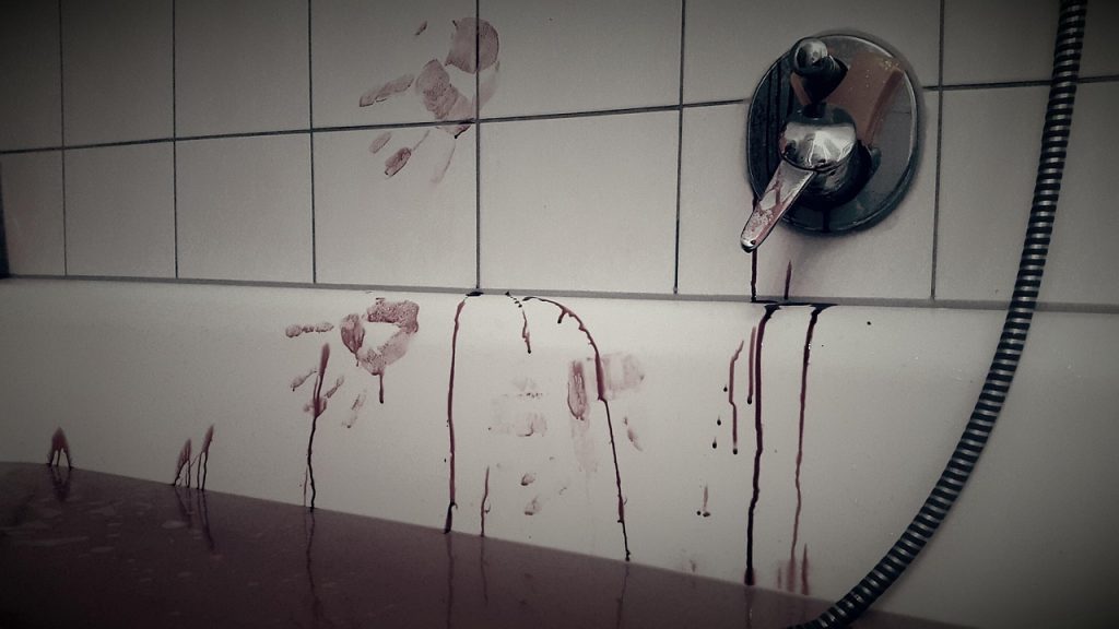 A gruesome scene reminiscent of serial killers' crimes, showing a white tiled bathroom wall and bathtub heavily smeared with blood. Dark red, viscous streaks drip down the tiles and the side of the tub from multiple bloody handprints, including a distinct palm print. The water in the bathtub is disturbingly dark red, appearing to be filled with blood. A chrome faucet and shower hose are visible on the wall, with blood also dripping from the faucet. The image evokes a strong sense of violence and horror.