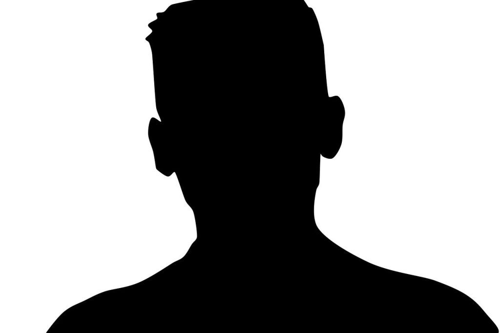 A black silhouette of a person's head and shoulders is centered on a plain white background. The silhouette is sharply defined, showing the outline of a short haircut and the broad shape of the shoulders, without any discernible facial features or clothing details.