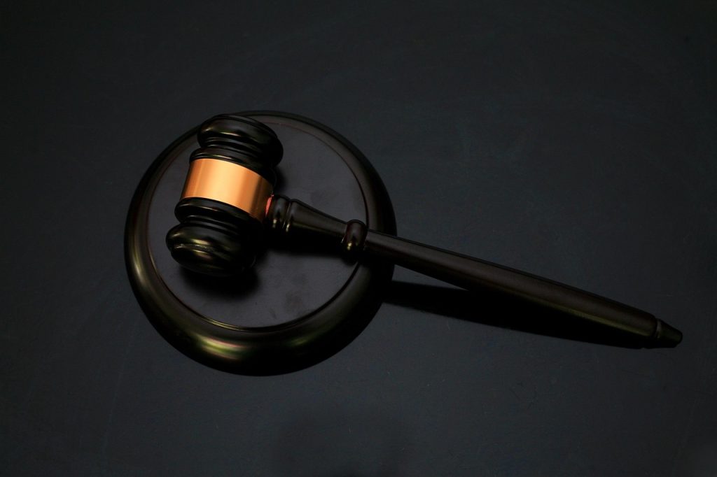 A close-up of a wooden gavel with a copper-colored band resting on a black circular block, set against a dark background.