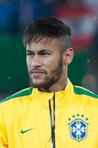 Close-up of Neymar Jr looking sideways wearing a yellow Brazil CBF track jacket during a rainy international match in 2014.