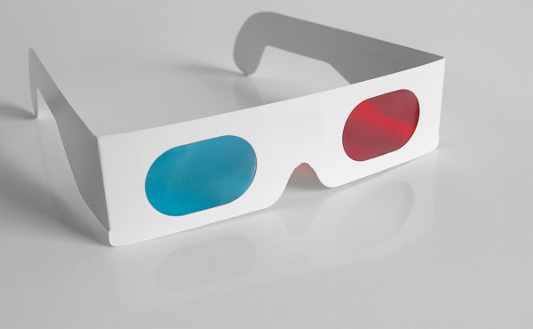 A pair of classic retro 3D glasses with white cardboard frames, featuring one blue lens and one red lens, resting on a glossy white surface. These surfaced just when television seemed unstoppable.