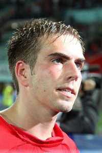 Close-up profile of Philipp Lahm, one of football's legendary captains, looking intently off-camera with wet hair, wearing a red jersey.